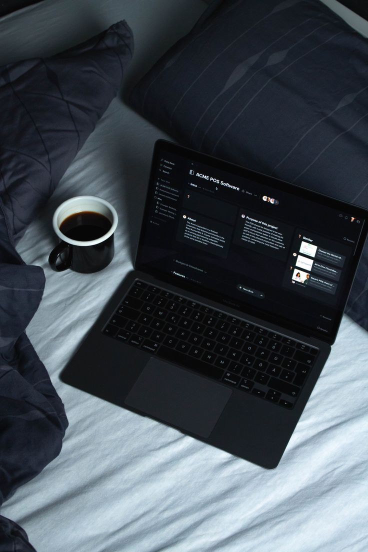 MacBook Air on a bed next to a cup of fresh coffee